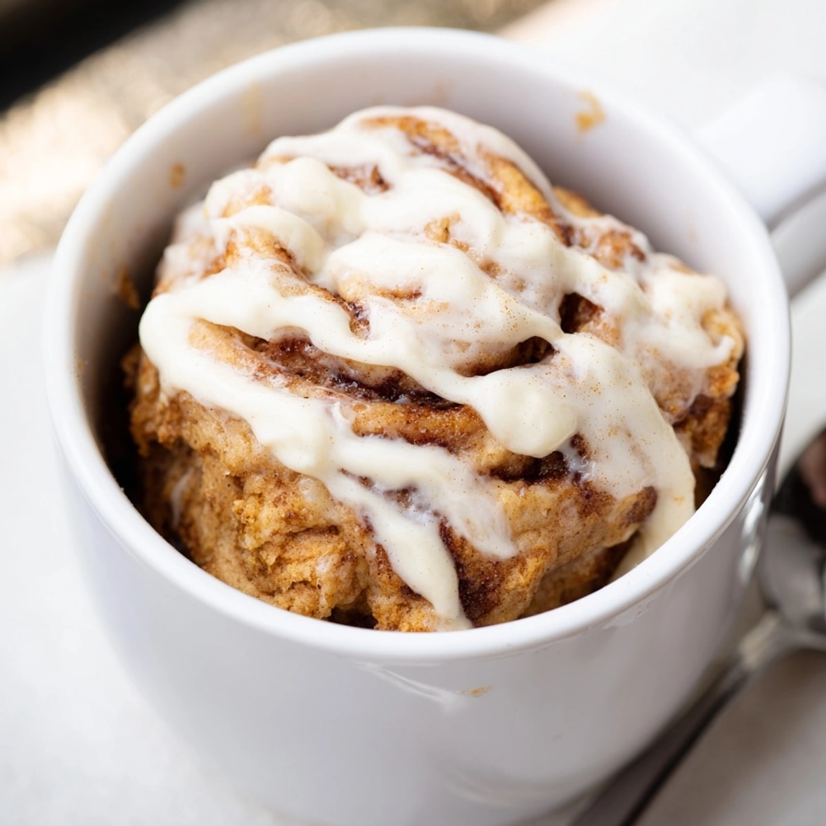 Close-up of a freshly microwaved Protein Cinnamon Roll Mug Cake with a decadent swirl.