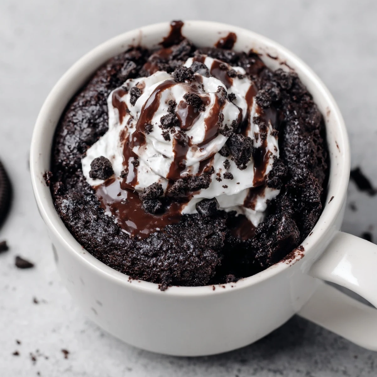 A close-up of a warm, fudgy Oreo mug cake, showing rich chocolate and cookie crumb texture.
