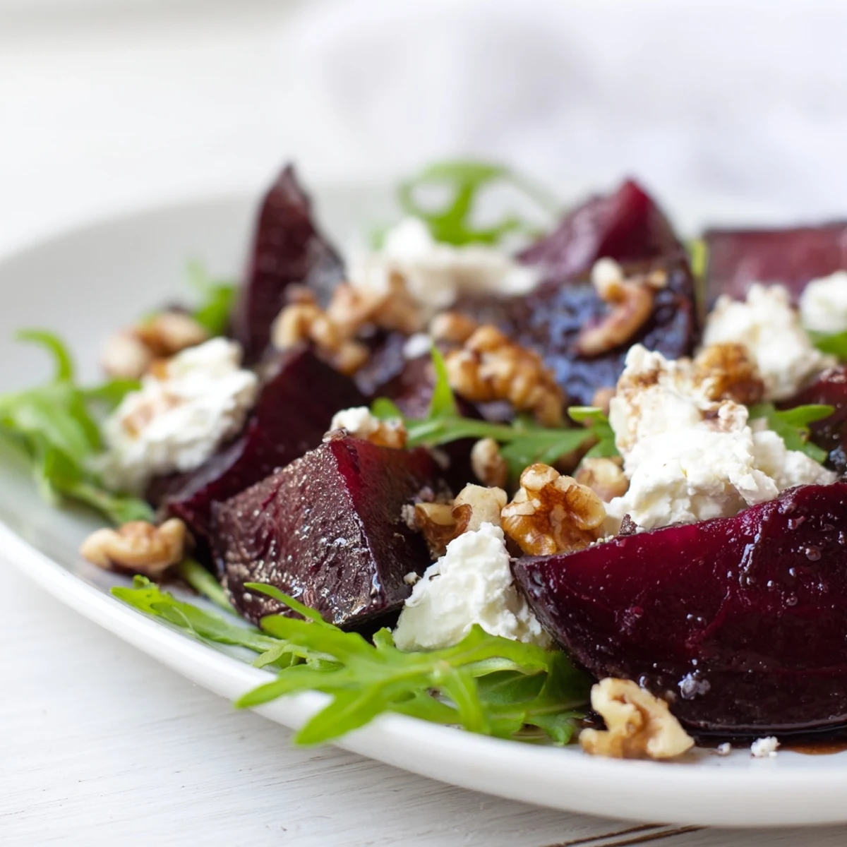 The Roasted Beet Goat Cheese Salad is drizzled with glossy balsamic vinaigrette and garnished with fresh chives on a rustic plate.  