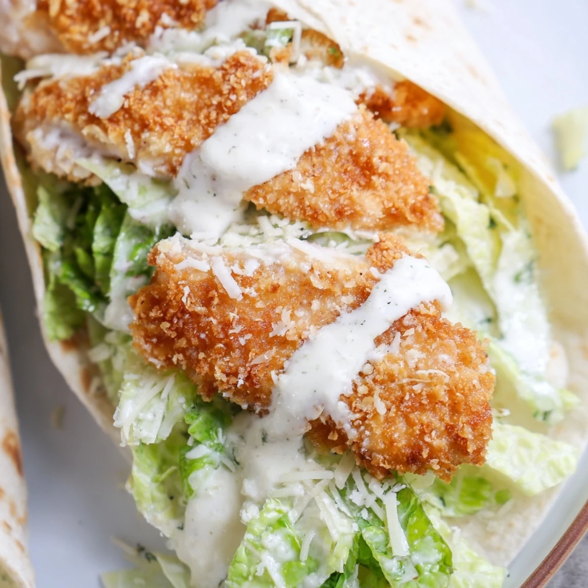 Homemade Crispy Chicken Caesar Wrap cut in half to reveal tender fried chicken, vibrant romaine, and creamy dressing inside a warm tortilla.