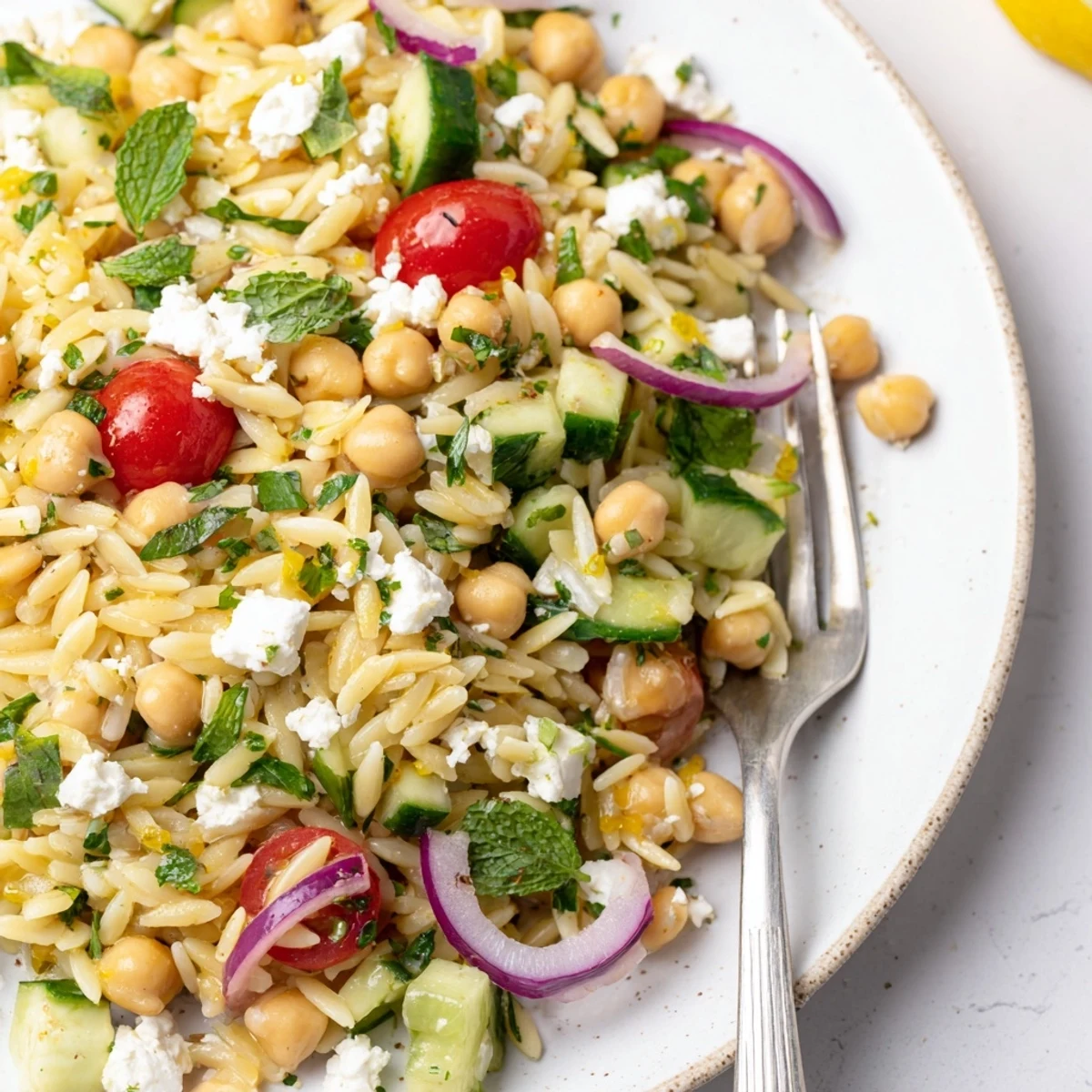 A top-down view of Lemony Chickpea Orzo Salad in a white bowl, featuring tender orzo pasta, protein-rich chickpeas, diced cucumber, and halved cherry tomatoes.