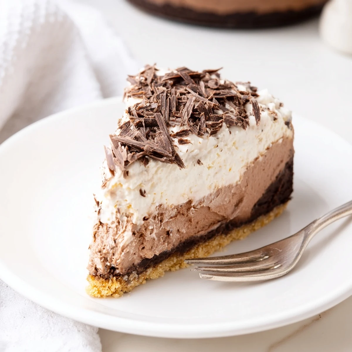A rich slice of Lighter Chocolate Cottage Cheese Cheesecake, topped with dark chocolate shavings and a creamy dollop of Greek yogurt.