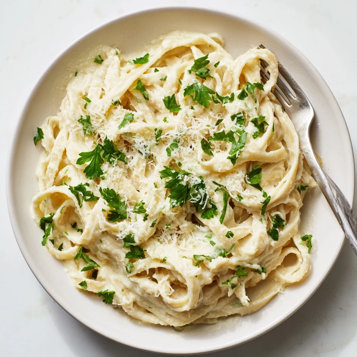Creamy Easy Creamy Cauliflower Alfredo pasta twirls on a fork, garnished with fresh parsley and extra Parmesan.