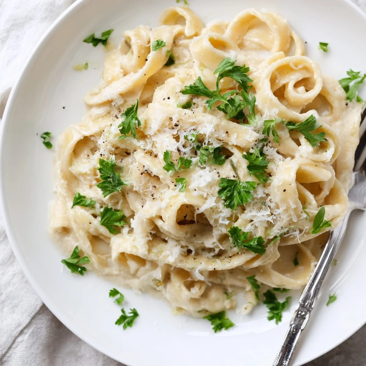 A bowl of Easy Creamy Cauliflower Alfredo features fettuccine coated in a velvety sauce, steaming gently.