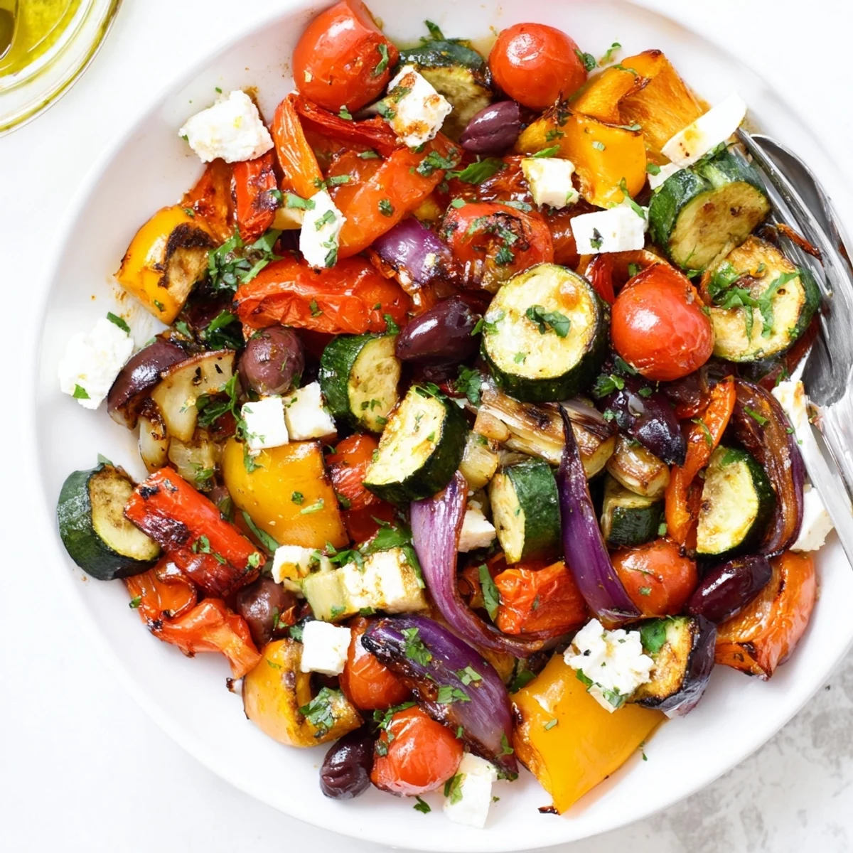 A close-up of Roasted Greek Salad showcases warm, caramelized vegetables, feta cubes, Kalamata olives, and fresh parsley on cucumber slices.  