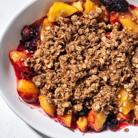 Warm, bubbly fruit crisp with golden oat topping, featuring a generous serving of fresh fruit.
