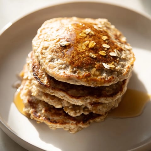 Golden brown banana oat pancakes stacked high, ready to enjoy with fresh fruit and syrup.
