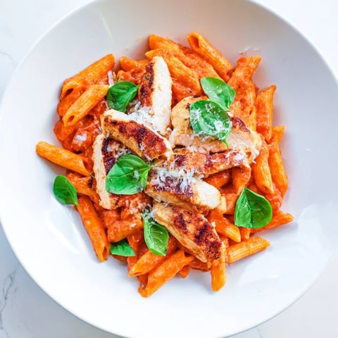 Sizzling strips of seared chicken nestle over penne in a vibrant, zesty chili-infused tomato sauce for a hearty meal.