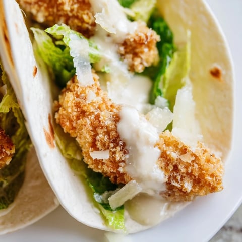 Golden crispy chicken strips nestled in a soft flour tortilla with fresh romaine, Parmesan, and creamy Caesar dressing for a satisfying meal.  
