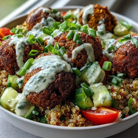 Golden-brown baked falafel rests atop fluffy quinoa with cucumber, tomatoes, and green onions, drizzled with creamy garlic tahini sauce.