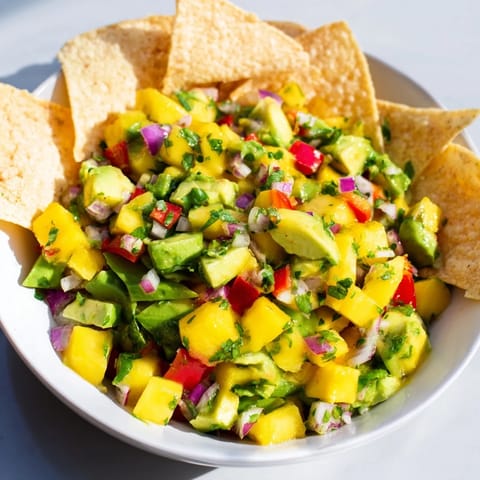 Refreshing mango avocado salsa, bursting with flavors, paired with crunchy tortilla chips.  