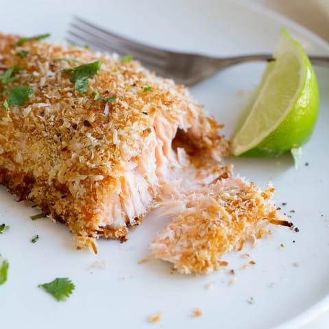 Savory Coconut Crusted Salmon sits on a plate, showcasing crunchy tropical textures and vibrant colors.  