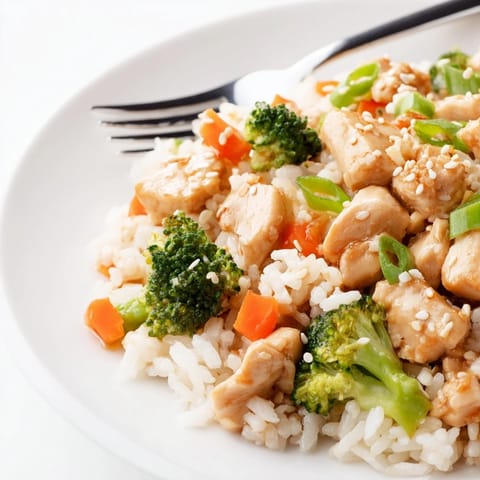 A spoon lifts a bite of One Pan Honey Garlic Chicken Broccoli Rice from the skillet, revealing tender meat and glistening sauce.  
