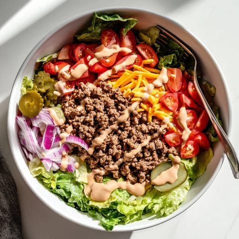 Hearty ground beef, fresh vegetables, and melted cheddar cheese top a vibrant bed of lettuce in this Easy Big Mac in a Bowl recipe, ready for a quick dinner.  