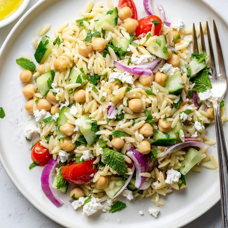 A vibrant Mediterranean-inspired Lemony Chickpea Orzo Salad in a shallow serving dish, garnished with fresh parsley and mint, perfect for a light meal.