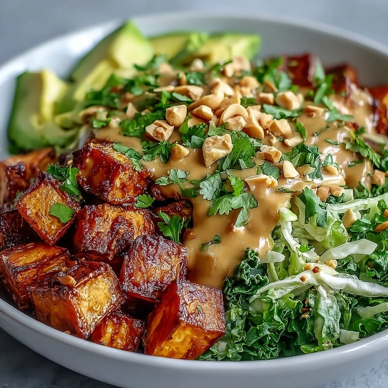 Drizzled creamy Thai Peanut Sweet Potato Buddha Bowl topped with chopped peanuts and cilantro, served alongside a small dipping bowl of peanut sauce.