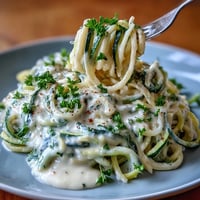 Creamy cottage cheese Alfredo sauce drizzled over fresh zucchini noodles, garnished with parsley and Parmesan.  