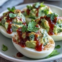 Creamy avocado deviled eggs with a spicy Sriracha drizzle, perfect for healthy party appetizers or quick snacks.